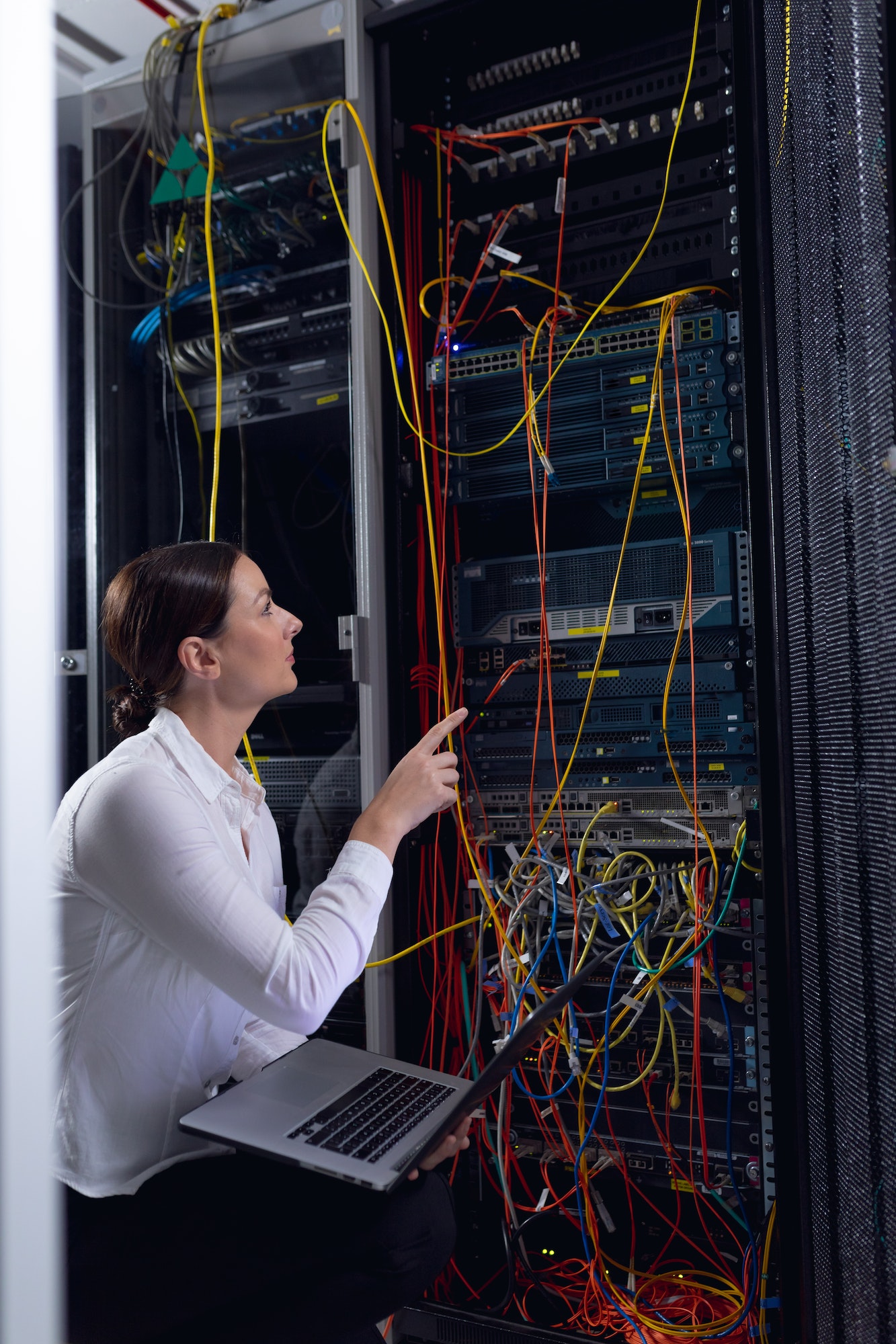 Caucasian female engineer with laptop inspecting computer server in computer server room